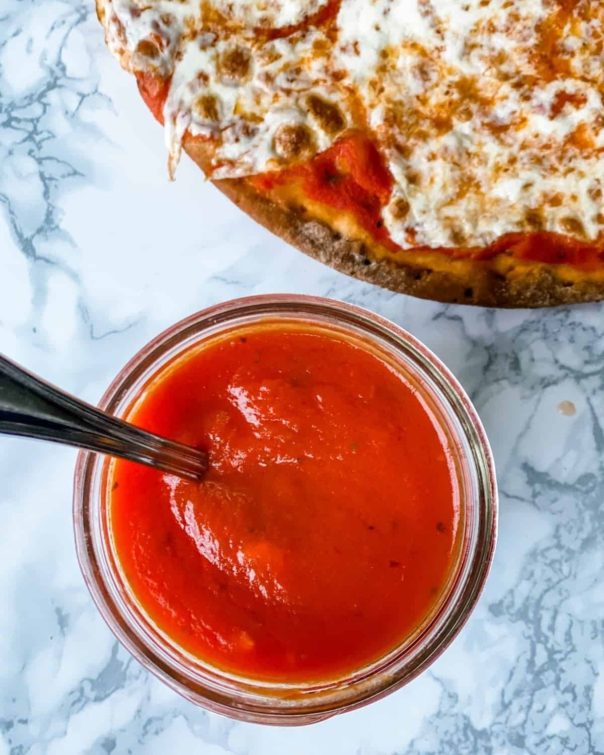 gluten-free pizza sauce in a mason jar next to pizza with cheese.