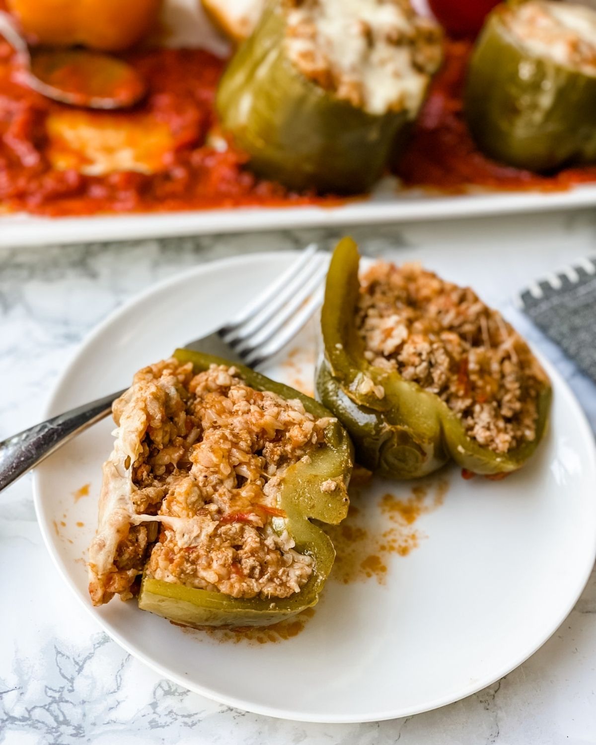 italian stuffed peppers cut in half on a plate with a pan of extra peppers in the background.