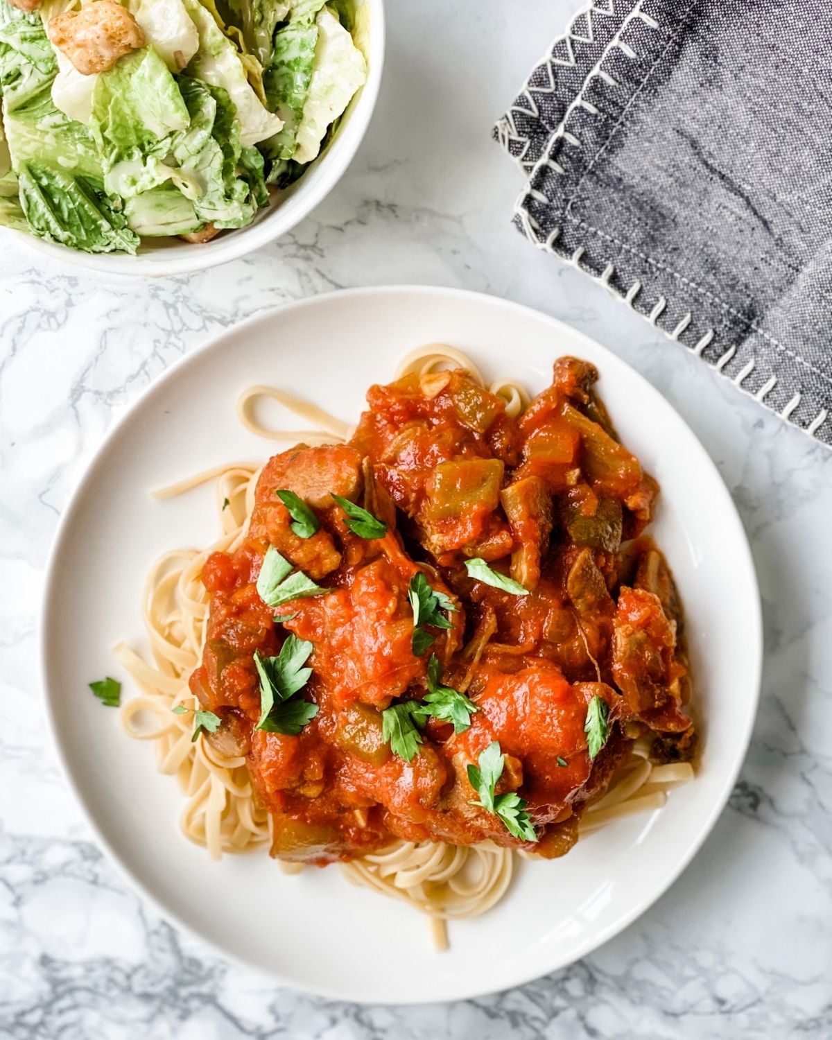 chicken cacciatore on a plate with gluten free pasta and side salad.