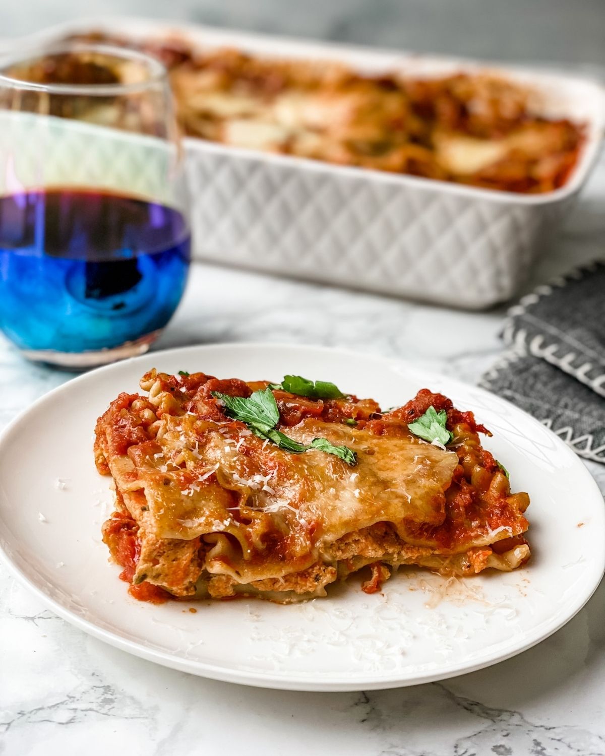 A piece of lasagna with a glass of wine behind it.