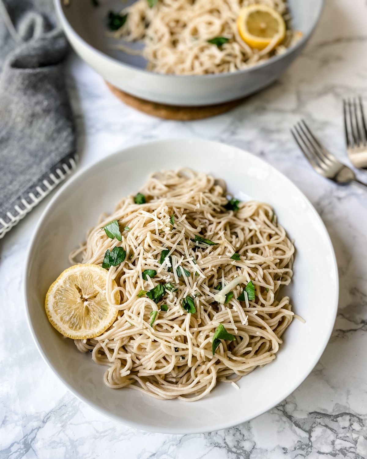 lemon garlic pasta on a plate with a pan of pasta in the background.