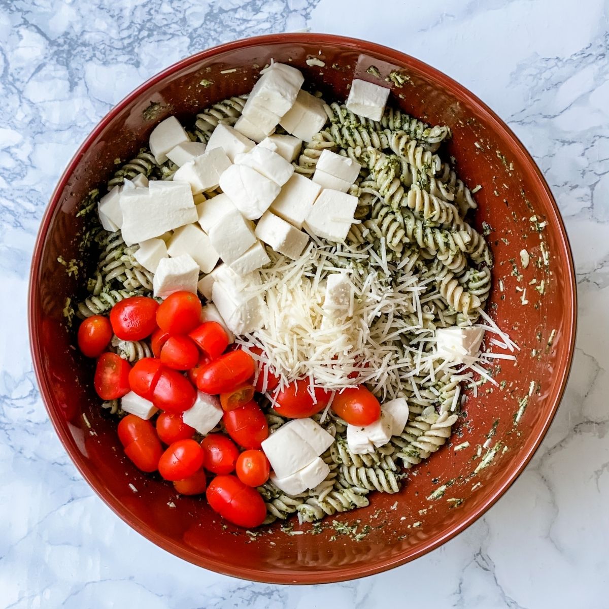tomatoes, fresh mozzarella, grated cheese in a bowl with pesto past.