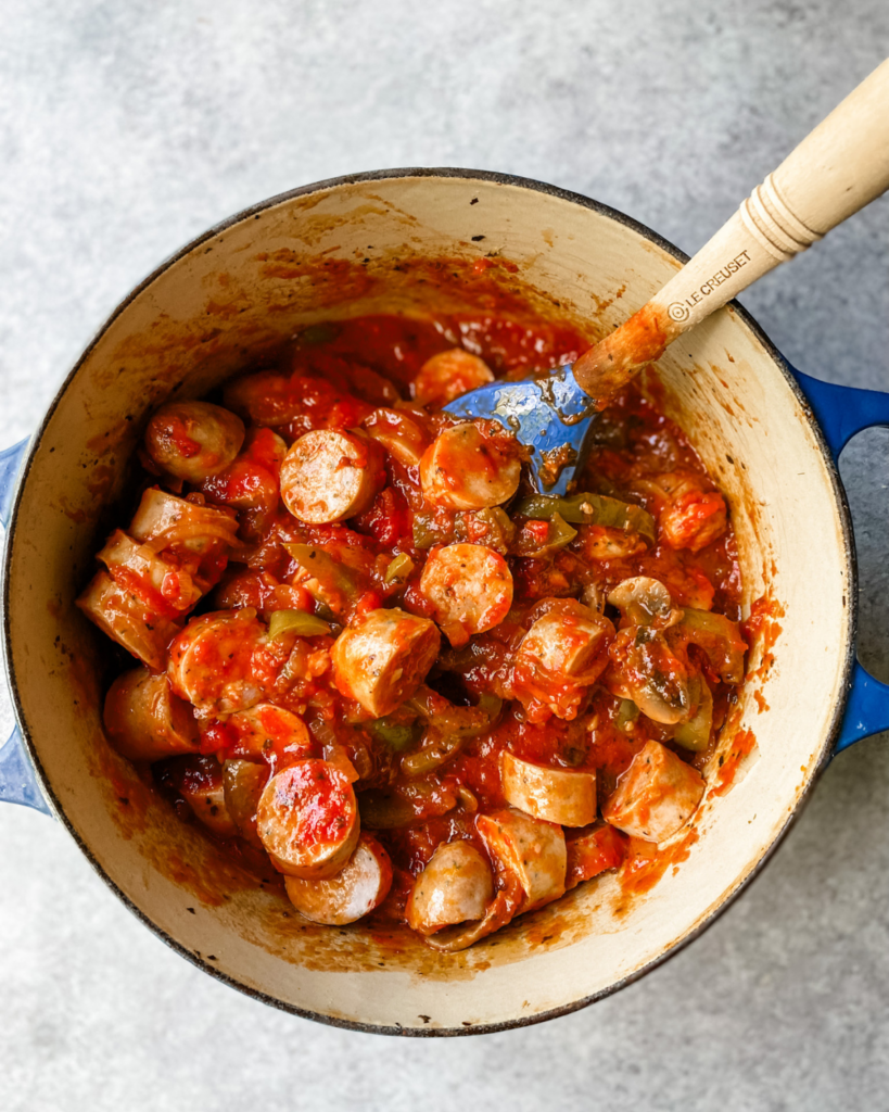 sliced sausage in pot with veggies and sauce.