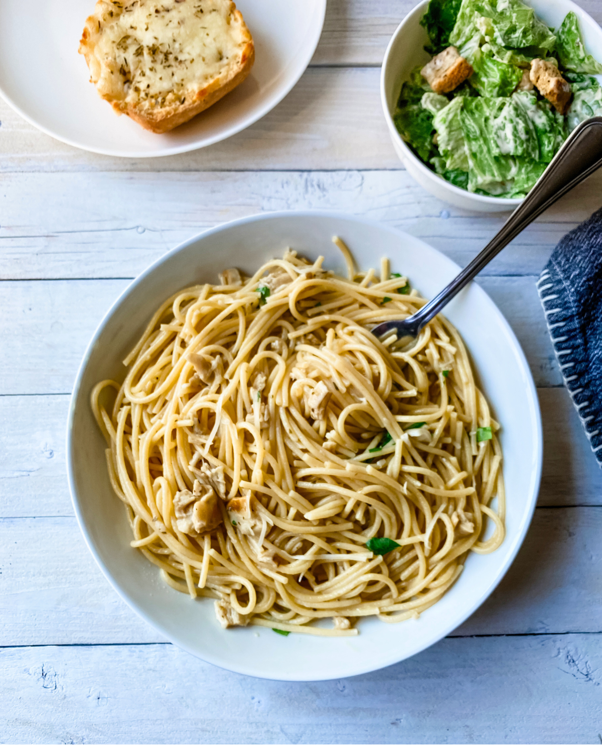 overhead picture of pasta with clam sauce twirled on a spoon and caesar salad and garlic bread in background