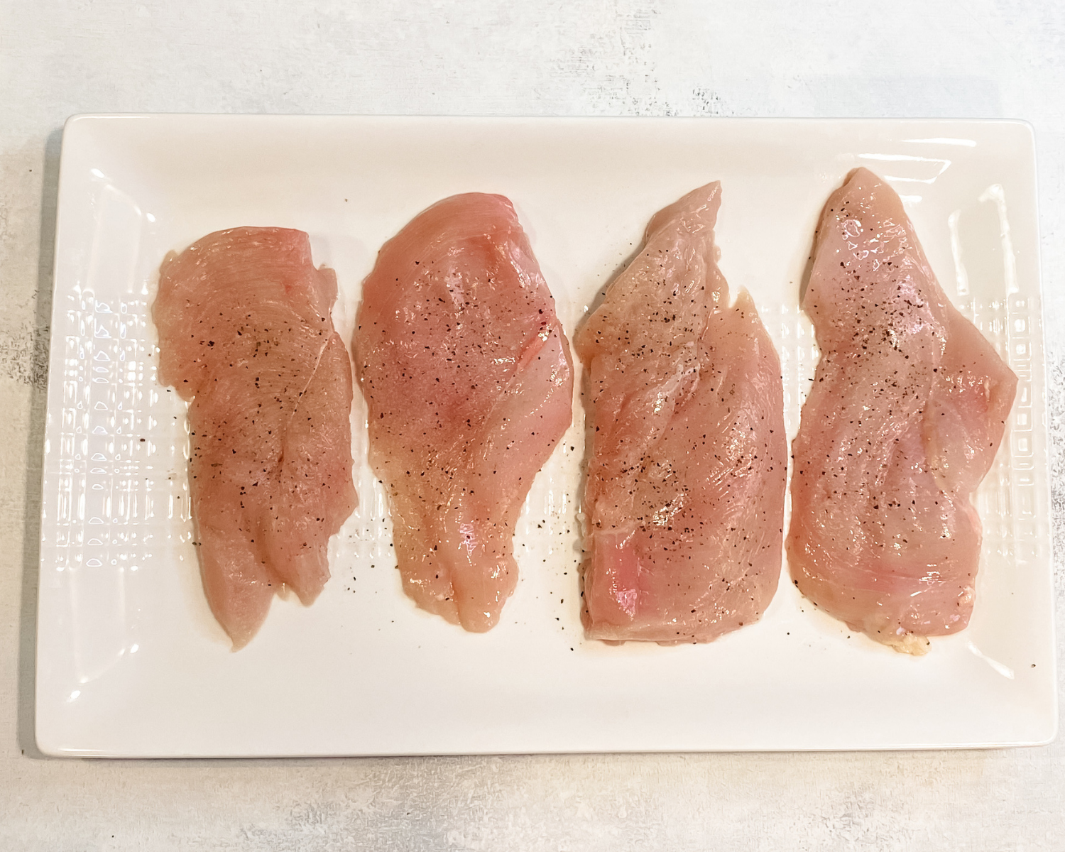 thinly slice chicken cutets on a white plater.