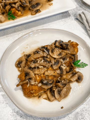 gluten free chicken marsala on a plate wit a platter in the background.